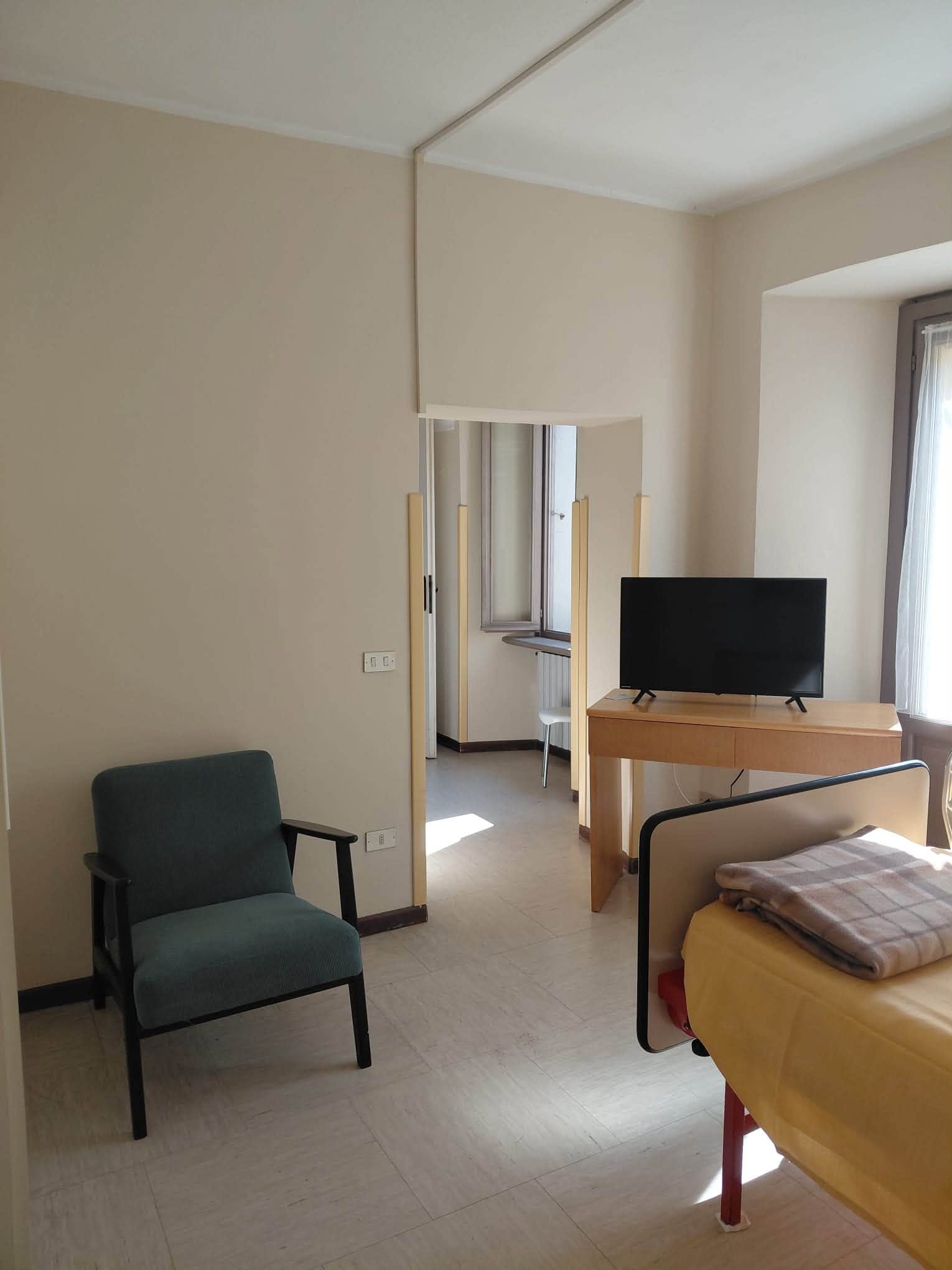 Un ambiente interno della residenza con una poltrona verde, una scrivania con il televisore e un letto